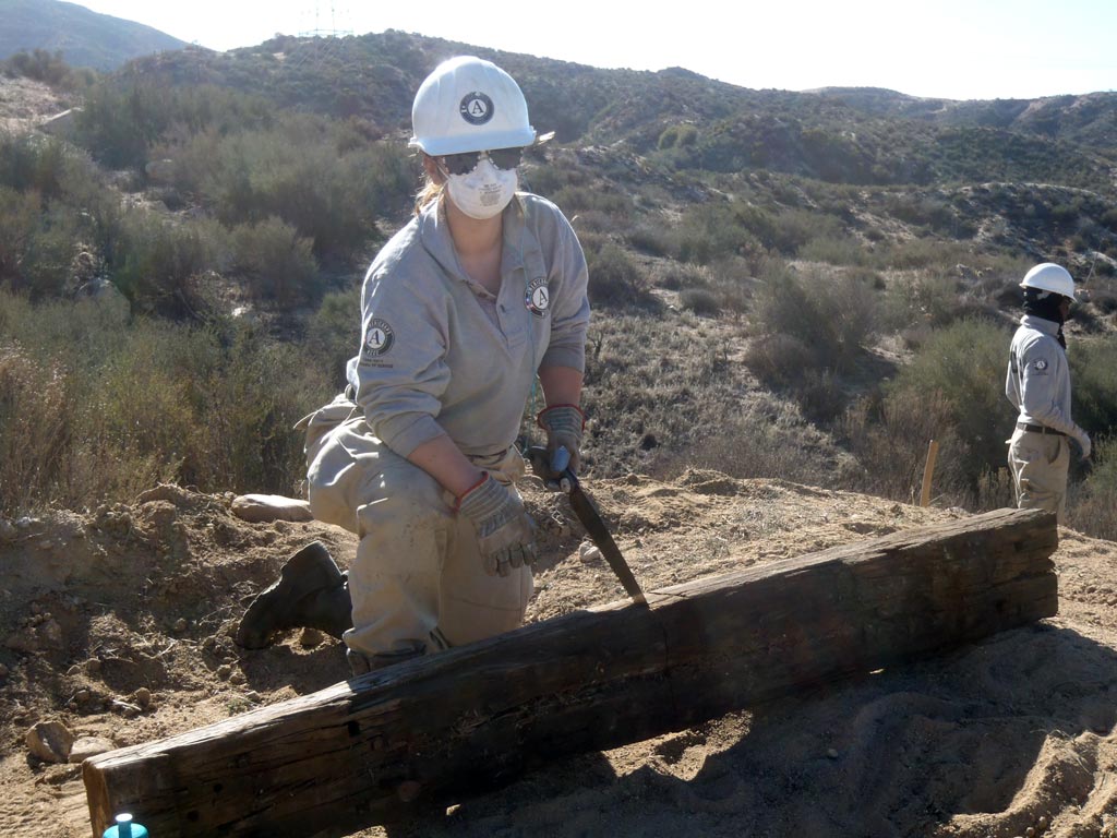 Kathleen Griffin sawing a timber to prepare it for placement on the trail.
