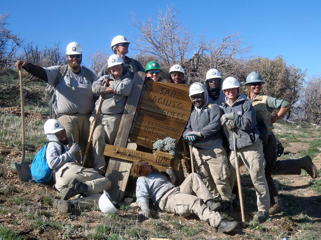 The entire crew posing, smiling (and chewing on the sign) at the San Jacinto Wilderness sign. Heidi Brill is on the far right.