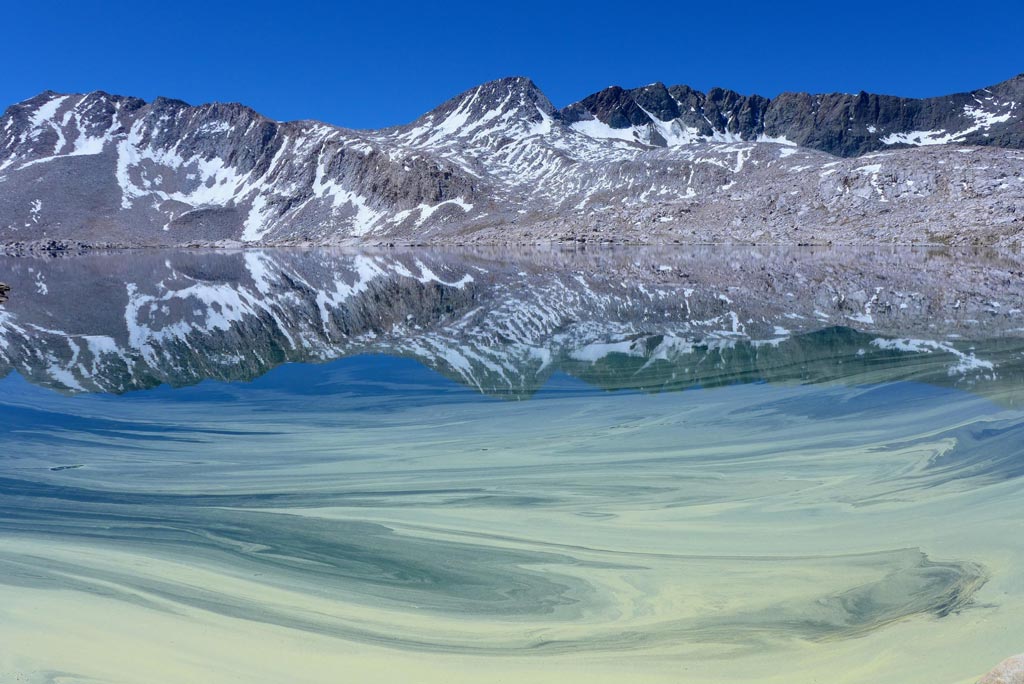 Pollen paints the glassy surface of Wanda Lake on a clear, brilliant July day. Photo by: Melody Shah