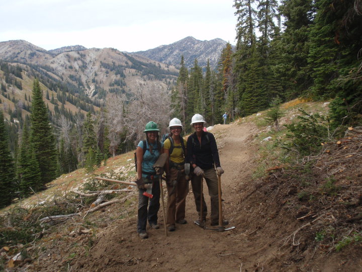 Three people pose on a dirt trail with mountains in the background