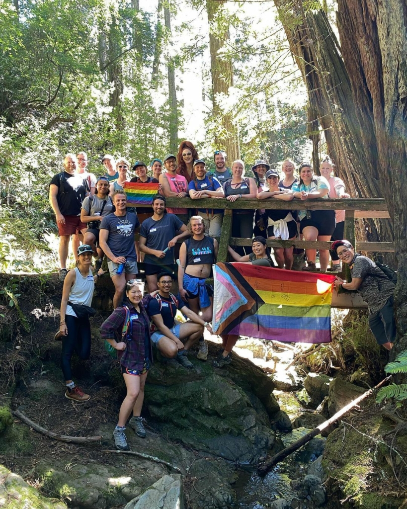 A group of people pose with a large Pride flag in the forest