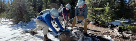 PCTA volunteers work together to move a rock in the snow