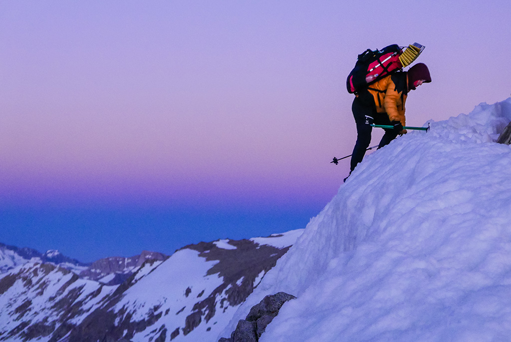 Under the colors of a pre-dawn sky, Kristine Fry uses her ice-axe to climb up and over a wall of snow blocking the trail on her final push to Forester Pass. This photo was taken at the top of Forester Pass looking south on the morning of June 23, 2019.Photo by: Eddie O'Leary